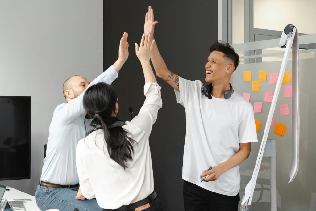 Diverse team members in an office high-fiving, symbolizing success and teamwork in a supportive environment.